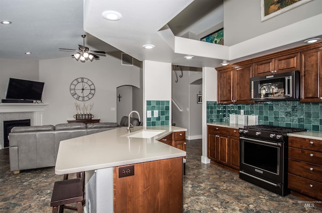 kitchen with sink, a kitchen bar, a brick fireplace, gas stove, and a center island with sink