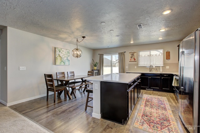 kitchen with visible vents, light wood-style flooring, dark cabinetry, freestanding refrigerator, and light countertops