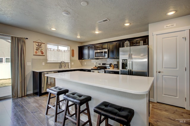 kitchen featuring wood finished floors, visible vents, a sink, stainless steel appliances, and a kitchen breakfast bar