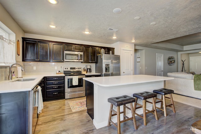 kitchen with visible vents, a breakfast bar, a sink, light wood-style floors, and appliances with stainless steel finishes