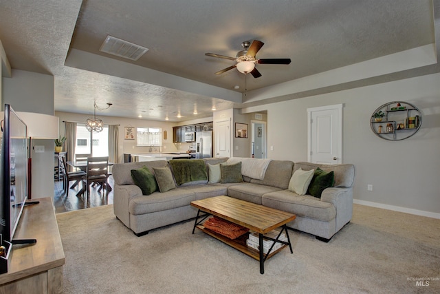 living area featuring baseboards, visible vents, a tray ceiling, ceiling fan, and light colored carpet