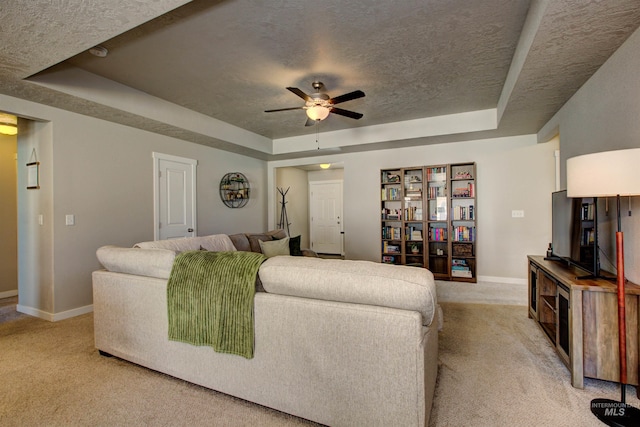 living area with a raised ceiling, a textured ceiling, and light carpet