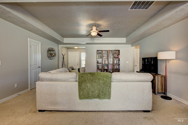 carpeted living room with visible vents, baseboards, and a tray ceiling