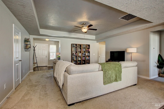 living area with visible vents, baseboards, a tray ceiling, ceiling fan, and light carpet