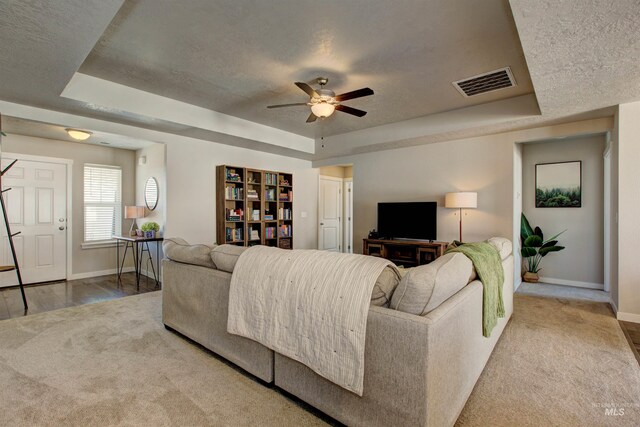 living area featuring visible vents, a raised ceiling, and baseboards