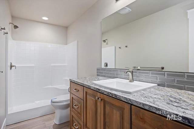 full bathroom featuring toilet, vanity, tiled shower, and wood finished floors