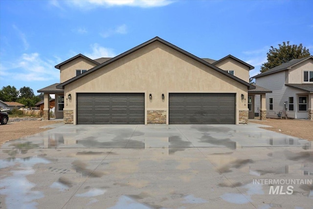 view of front of house with a garage, stone siding, concrete driveway, and stucco siding