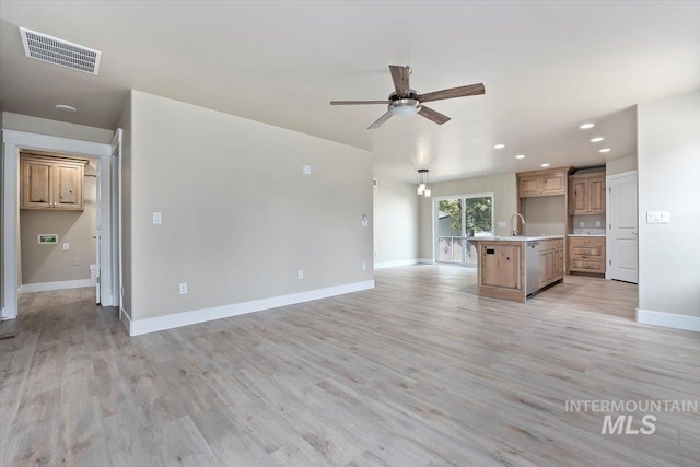 unfurnished living room featuring visible vents, a sink, ceiling fan, light wood-type flooring, and baseboards