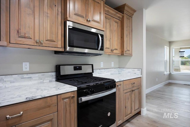 kitchen featuring gas range oven, stainless steel microwave, brown cabinetry, and baseboards