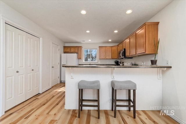 kitchen with brown cabinets, white fridge with ice dispenser, a peninsula, a breakfast bar area, and light wood finished floors