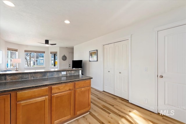 kitchen with light wood-type flooring, dark stone counters, recessed lighting, ceiling fan, and brown cabinets