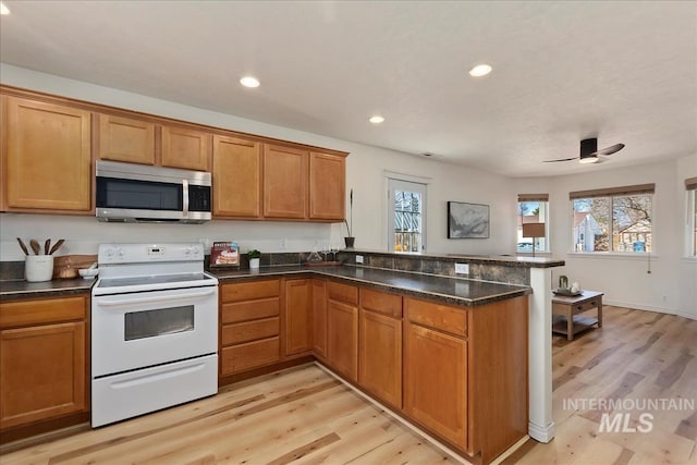 kitchen with stainless steel microwave, plenty of natural light, white electric range oven, and a peninsula