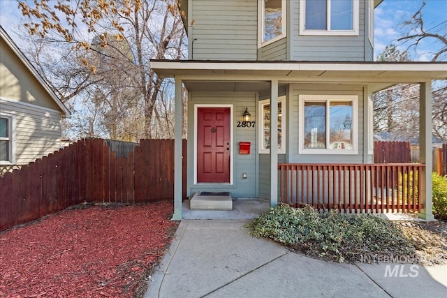 view of exterior entry featuring a porch and fence