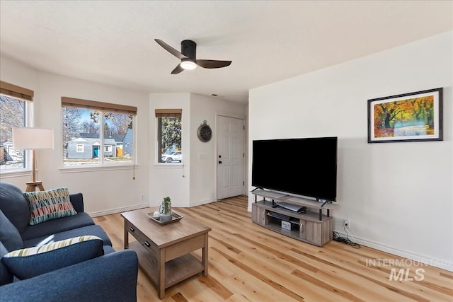 living area with plenty of natural light, a ceiling fan, baseboards, and light wood finished floors