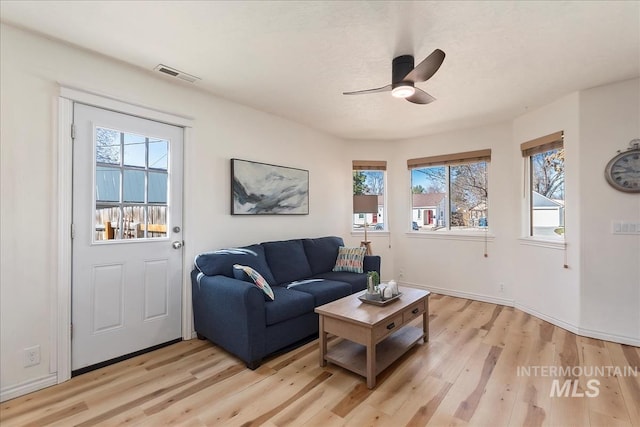 living room featuring baseboards, a ceiling fan, visible vents, and light wood-type flooring