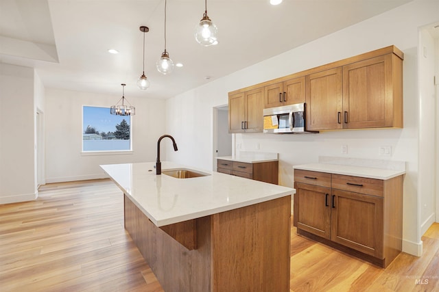 kitchen featuring decorative light fixtures, sink, a center island with sink, and light hardwood / wood-style flooring