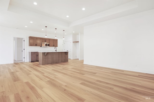 unfurnished living room featuring sink, a tray ceiling, and light hardwood / wood-style floors