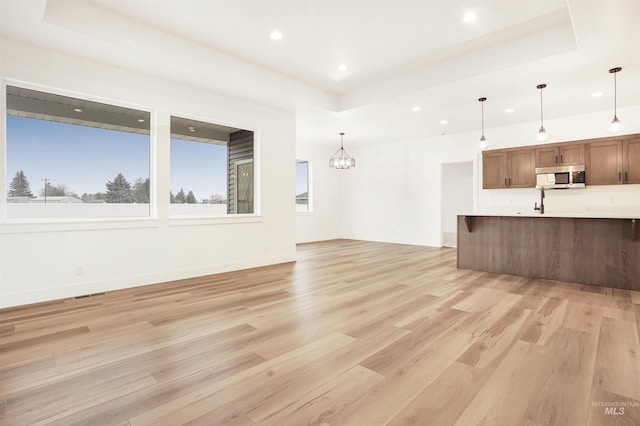 unfurnished living room featuring a raised ceiling, light hardwood / wood-style floors, and a notable chandelier