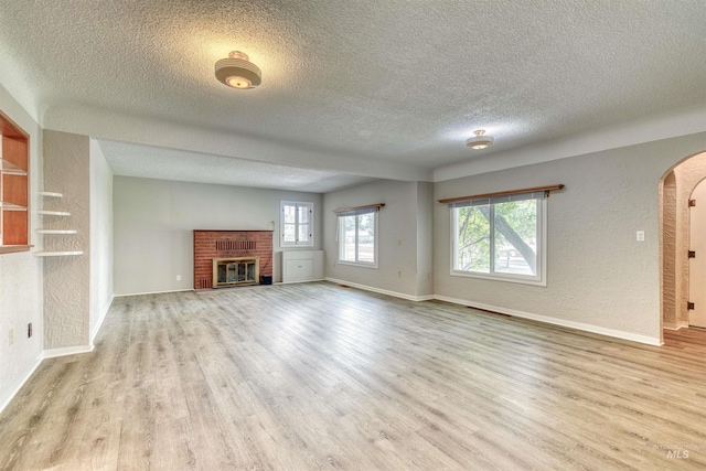 unfurnished living room with a textured ceiling, a fireplace, and light hardwood / wood-style flooring