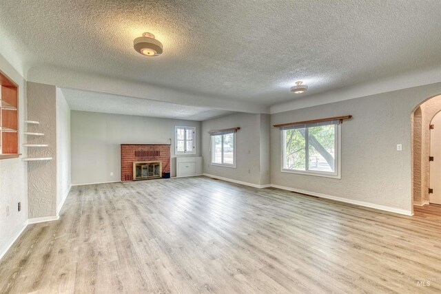 unfurnished living room featuring light hardwood / wood-style flooring, a brick fireplace, a textured ceiling, and plenty of natural light