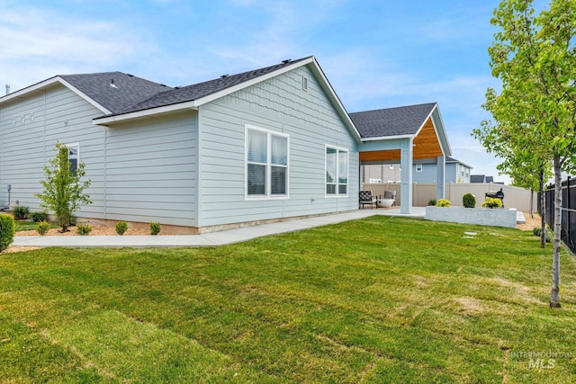 rear view of property featuring a lawn, a patio, fence, and a shingled roof