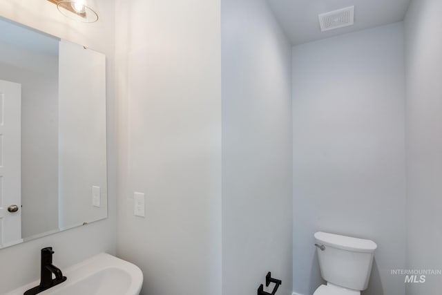 half bath featuring visible vents, toilet, and a sink