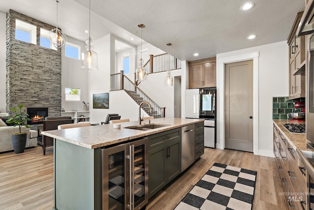 6071 S Pioneer Trail Way, Meridian, ID 83642 - kitchen featuring wine cooler, appliances with stainless steel finishes, a kitchen island with sink, light wood finished floors, and a fireplace