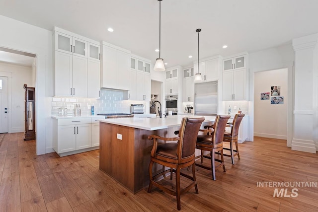 6706 Big Wood Way, Star, ID 83669 - kitchen with stainless steel appliances, tasteful backsplash, light countertops, a center island with sink, and light wood-type flooring