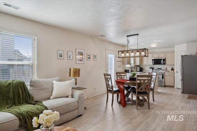 dining area featuring visible vents, a textured ceiling, and light wood-style floors