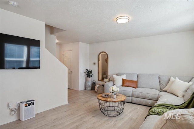 living room with baseboards, a textured ceiling, and light wood finished floors