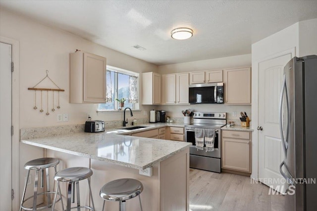 kitchen featuring stainless steel appliances, a peninsula, a sink, visible vents, and a breakfast bar area