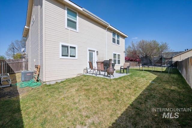 rear view of property featuring a patio area, a trampoline, central air condition unit, a lawn, and a fenced backyard