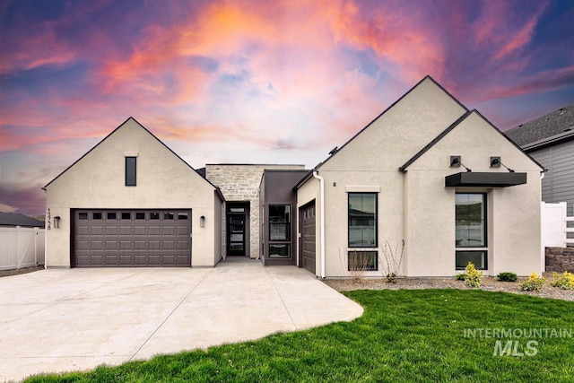 view of front of house featuring a lawn, fence, concrete driveway, an attached garage, and stucco siding