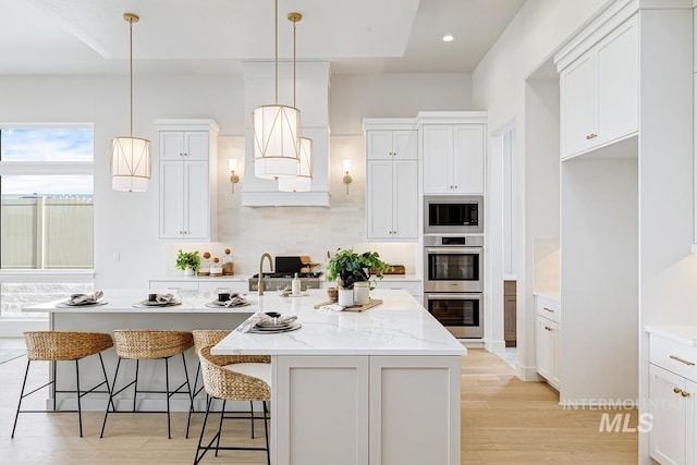 kitchen with tasteful backsplash, built in microwave, double oven, white cabinetry, and an island with sink