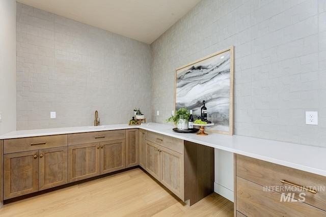 kitchen with light wood-type flooring, light countertops, a sink, and tile walls