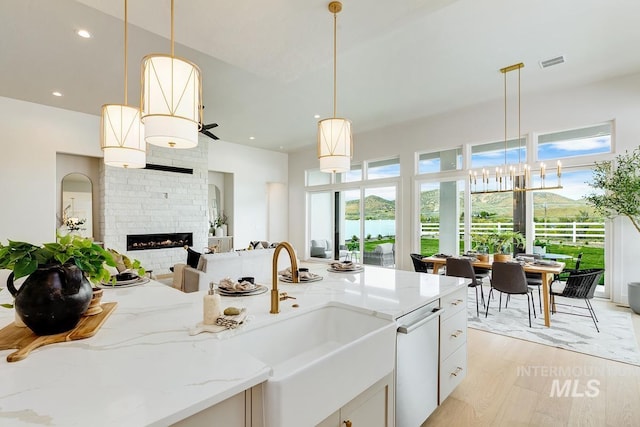 kitchen featuring light stone counters, a sink, a glass covered fireplace, open floor plan, and visible vents
