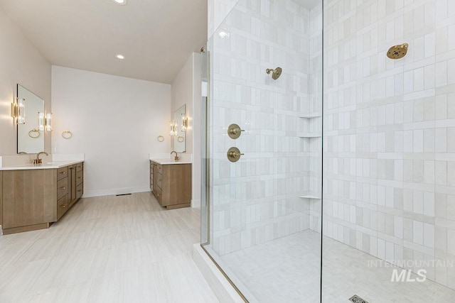bathroom with a walk in shower, baseboards, two vanities, and a sink