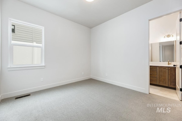 unfurnished bedroom featuring baseboards, ensuite bathroom, light carpet, and visible vents