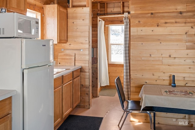 kitchen featuring light countertops, white appliances, wood walls, and brown cabinets