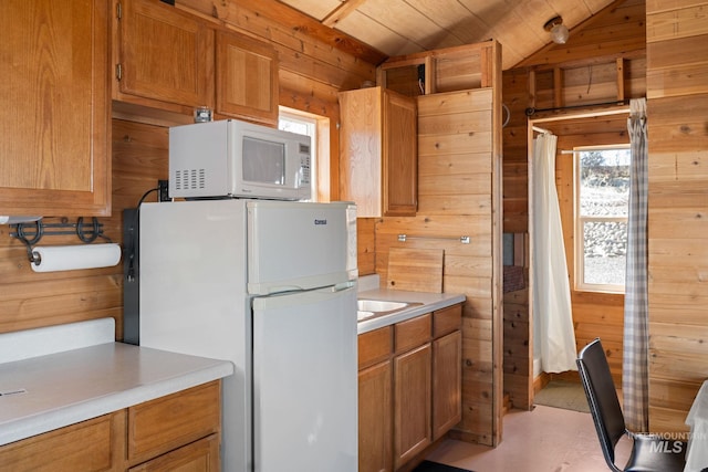 kitchen featuring white appliances, wooden walls, brown cabinets, vaulted ceiling, and light countertops