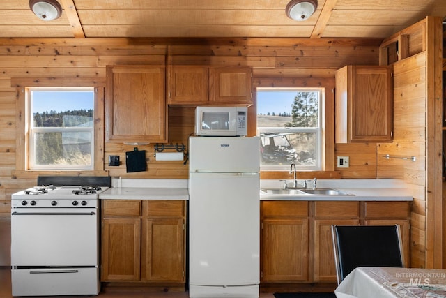 kitchen with wooden walls, white appliances, a sink, light countertops, and brown cabinets