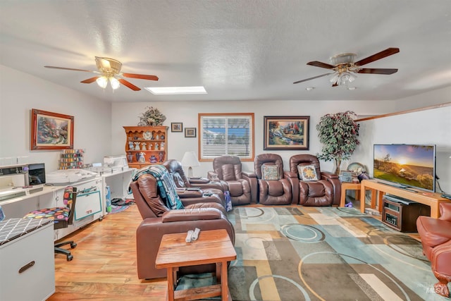 living room with a skylight, a textured ceiling, light hardwood / wood-style flooring, and ceiling fan