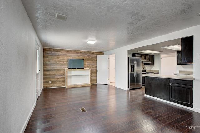 unfurnished living room featuring a textured ceiling, wooden walls, and dark hardwood / wood-style flooring