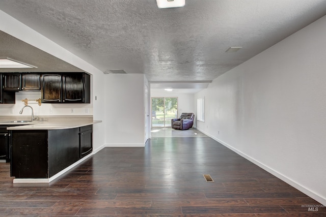 kitchen with a textured ceiling, dark wood-type flooring, kitchen peninsula, and sink