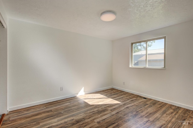 empty room with dark hardwood / wood-style flooring and a textured ceiling