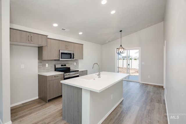 kitchen with sink, tasteful backsplash, decorative light fixtures, stainless steel appliances, and a kitchen island with sink