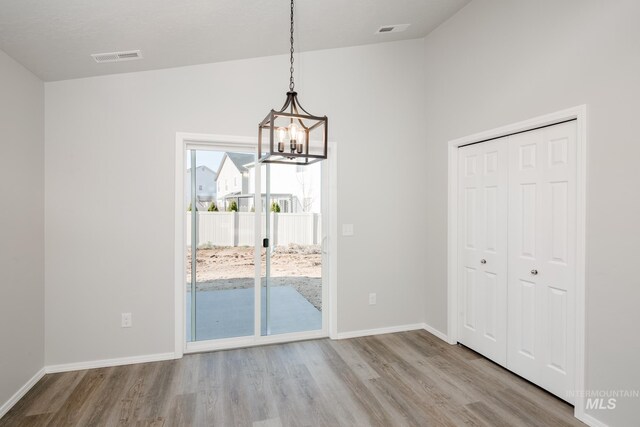 unfurnished dining area featuring vaulted ceiling, a chandelier, and light hardwood / wood-style floors