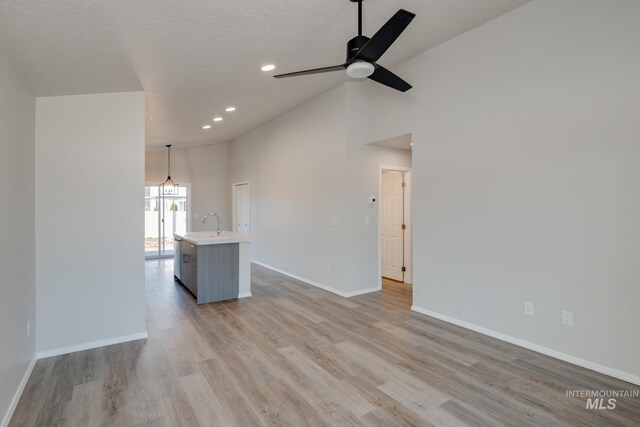 unfurnished living room with sink, light hardwood / wood-style flooring, ceiling fan, high vaulted ceiling, and a textured ceiling