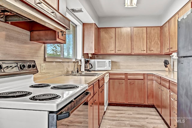 kitchen with custom range hood, backsplash, sink, light wood-type flooring, and white appliances