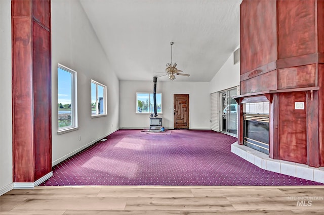 unfurnished living room with ceiling fan, plenty of natural light, a wood stove, and light carpet